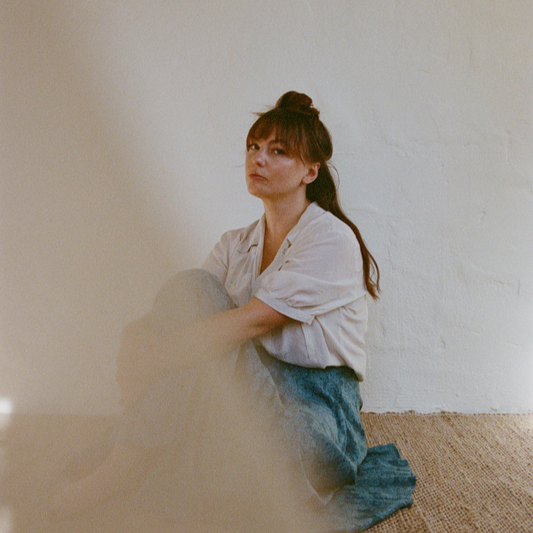 Angel Olsen seated against a pale wall.